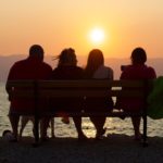 Vier Menschen sitzen auf der Bank und schauen dem Sonnenuntergang zu