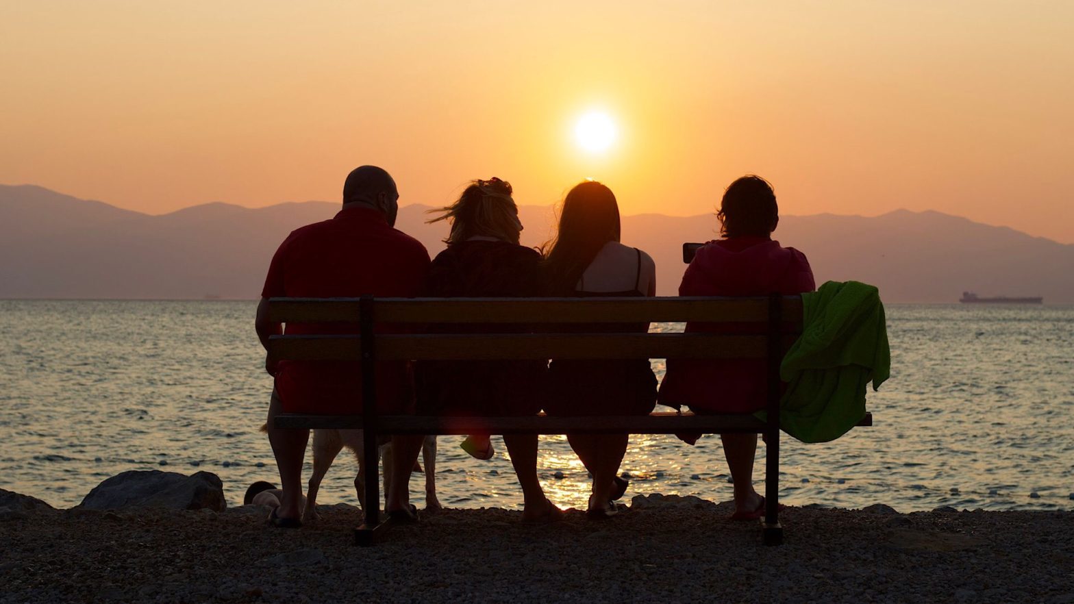 Vier Menschen sitzen auf der Bank und schauen dem Sonnenuntergang zu
