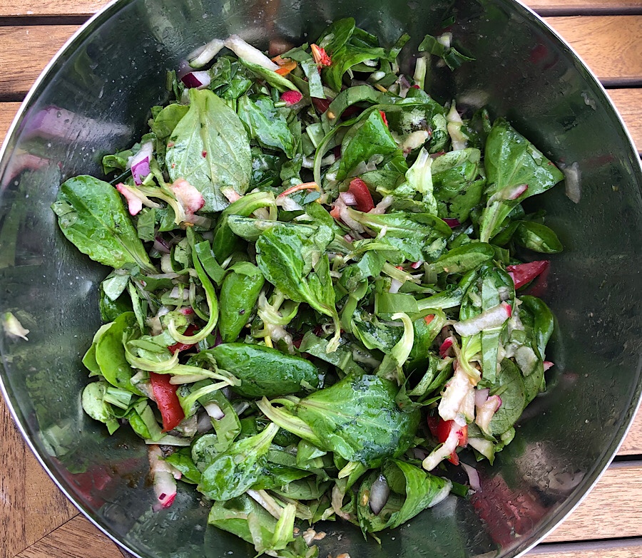 Grüner Salat mit geraspelten Gurken, Radieschen, Tomaten und roten Zwiebeln in einer Edelstahlschüssel. 