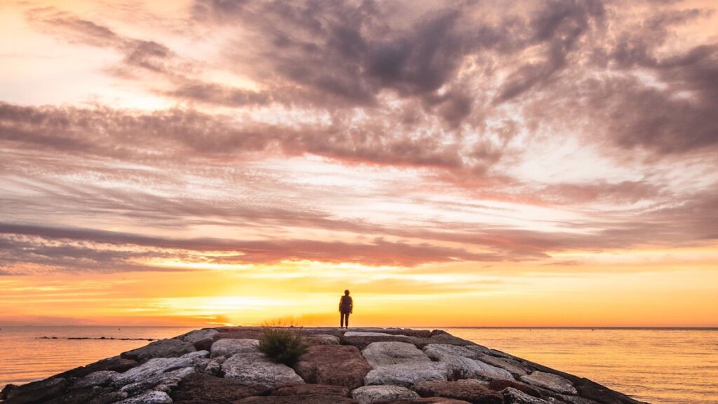 Ein Mensch steht vor dem Meer und beobachtet den spektakulären Sonnenaufgang