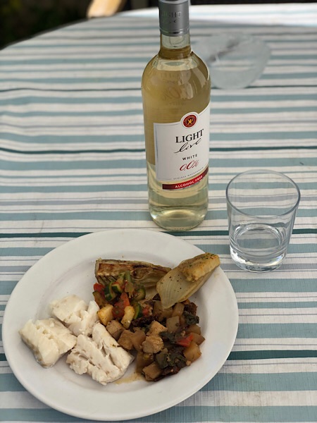 Ein Teller mit weißem Kabeljau, eine Flasche alkoholfreien Wein und ein Glas